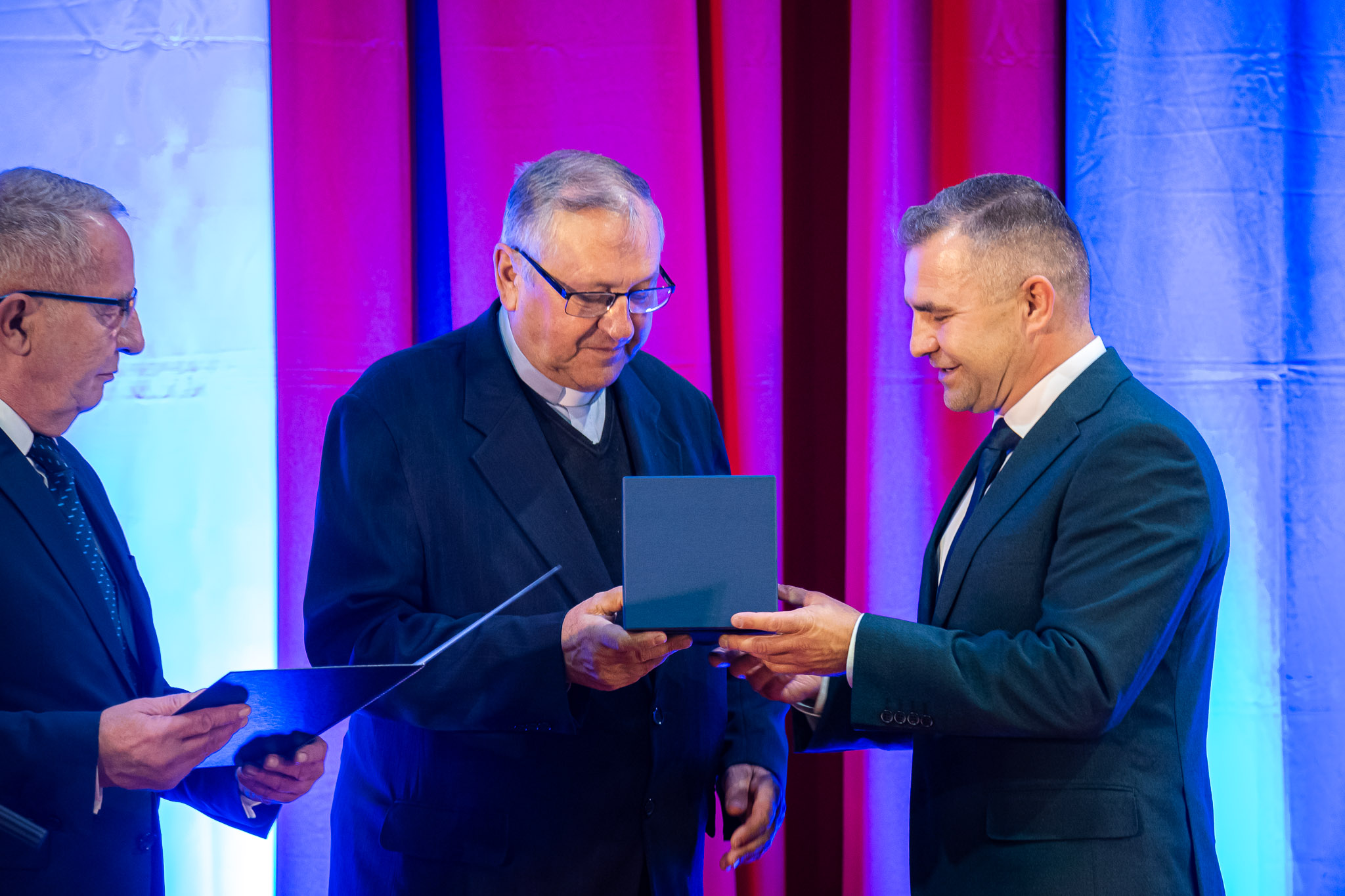 Ksiądz prałat Tadeusz Gut (w środku) odbiera medal z rąk burmistrza Michała Pasiecznego (z prawej) i przewodniczącego Rady Miejskiej Krzysztofa Woźniaka (z lewej)